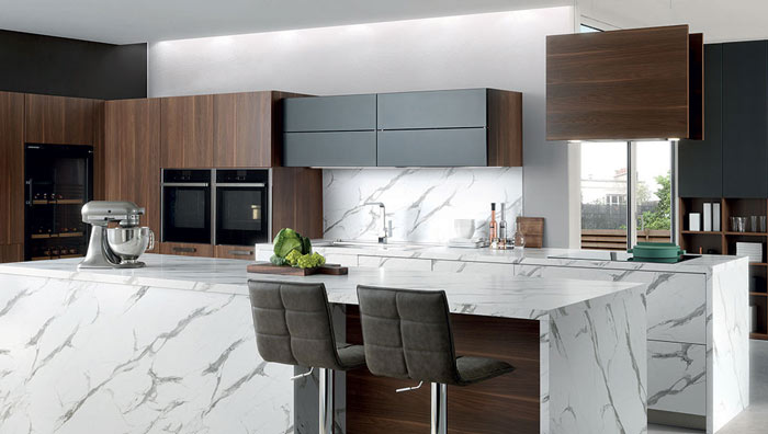 Vue zoomée de la cuisine Arcos Edition, composée d’un îlot central avec deux tabourets, les meubles en effet bois marron foncé et noir et le plan de travail effet marbre.