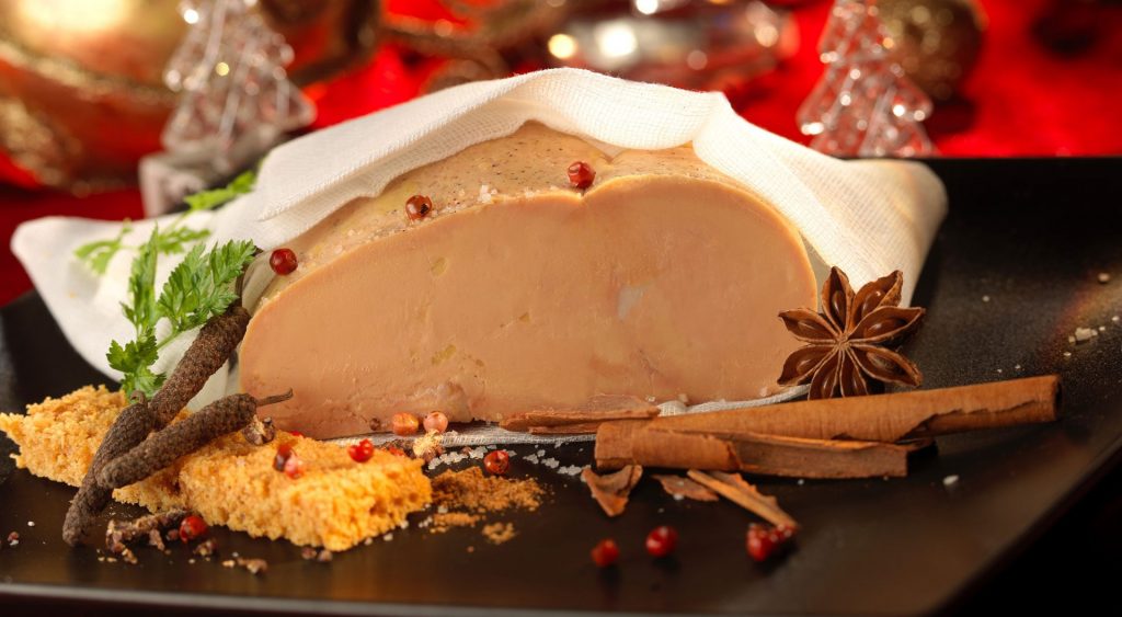 Foie gras maison enveloppé avec une gaze blanche et décoré avec des épices (grains de poivre rouge, cannelle, anis étoilé), de la fleur de sel, du pain et des mini pommes de pin.