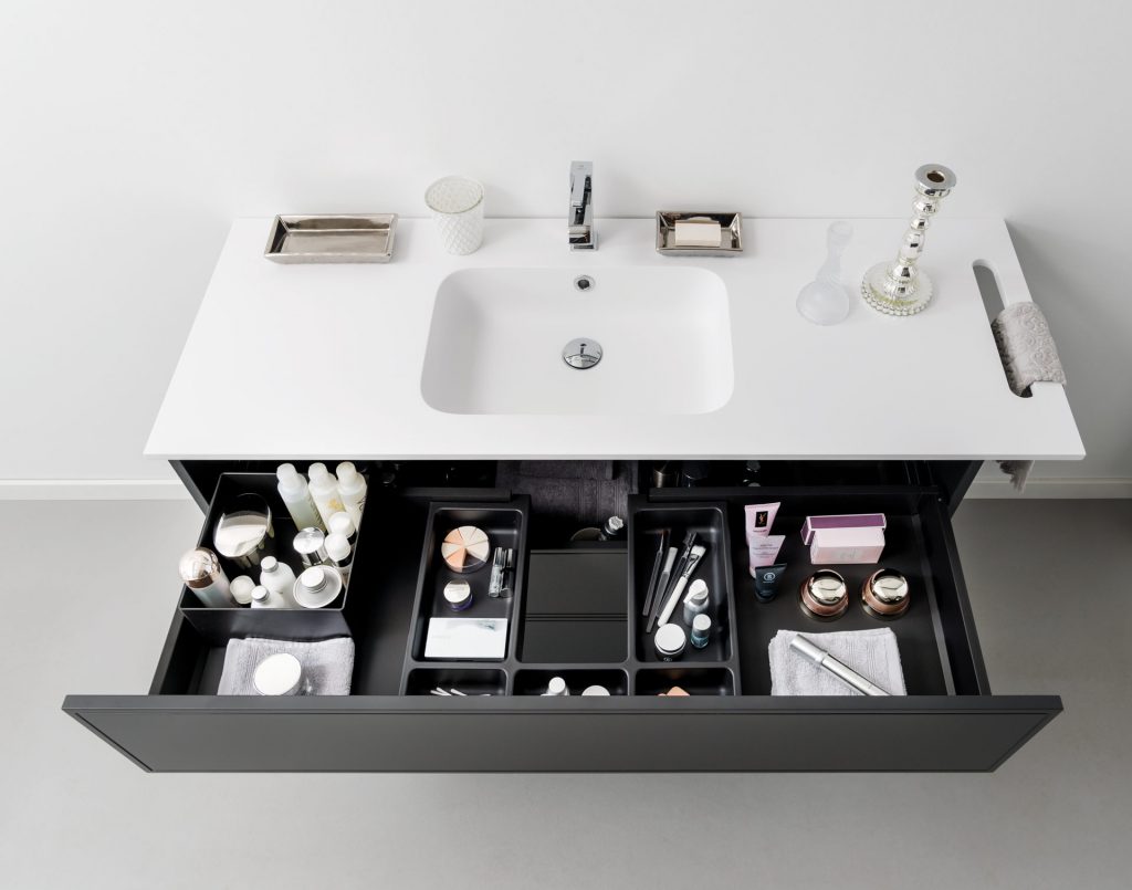 Vue de face du meuble bas sous vasque avec le bloc coulissant du haut ouvert et mis en situation avec des accessoires, modèle Boxea coloris gris foncé.