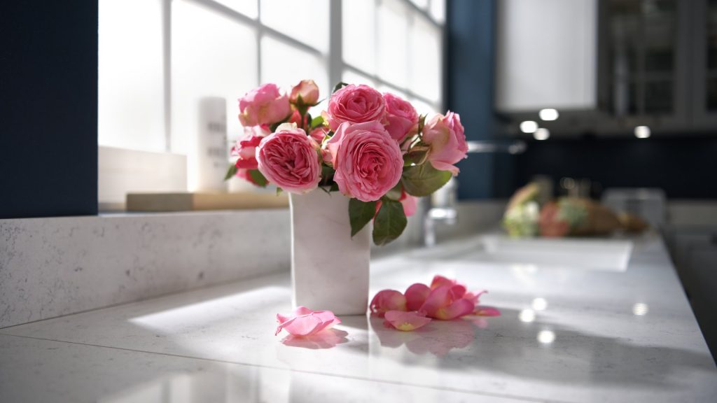 Un bouquet de roses dans un vase en céramique blanche et des pétales sur un plan de travail en quartz, orientation paysage.