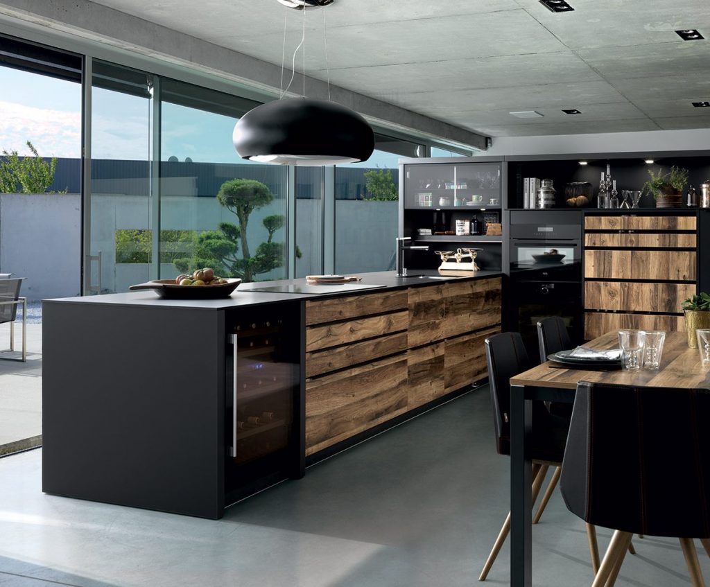 Vue d'ensemble de la cuisine design Arcos Edition avec les façades couleur marron clair effet bois et le plan de travail stratifié fin noir.