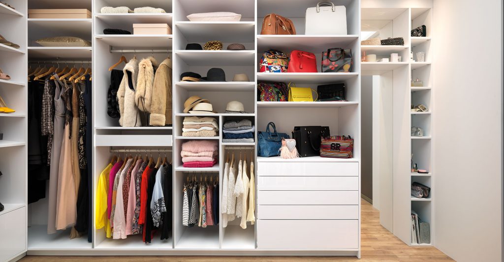Vue de l'intérieur d’un dressing : compartiments de rangement, étagères, penderies courtes, porte-pantalons, tiroirs coulissants, bloc coulissant et étagères pour sacs à main.