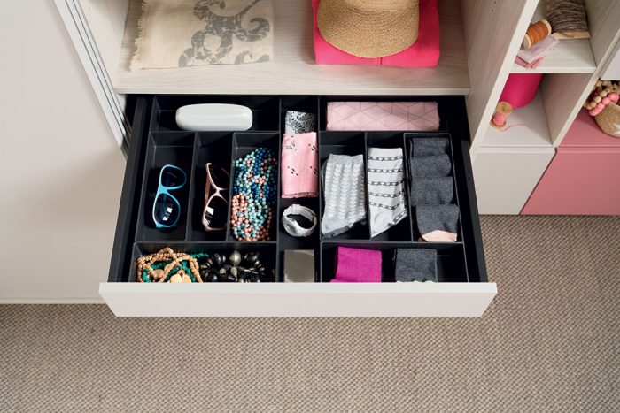 Vue de l’intérieur d’un tiroir ouvert organisé avec des boîtes de rangement dans le dressing Arcos coloris gris clair effet bois et Loft coloris rose et vert clair grisé.