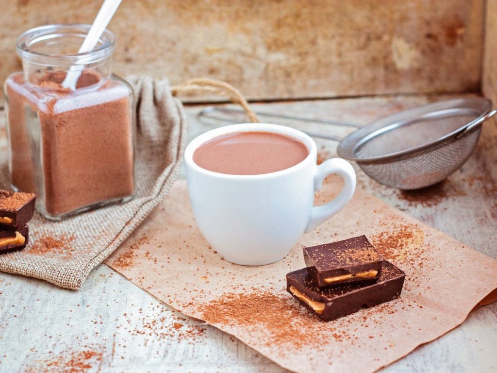 Vue d'une tasse de chocolat chaud posée sur une table avec un pot de chocolat en poudre et des carrés de chocolat.