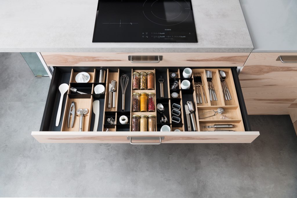 Vue d’en haut d’un tiroir ouvert avec le range couverts bois Latitude équipé d’accessoires de cuisine et d’épices, dans une cuisine Arcos coloris bois clair Ikori et Lazer coloris gris clair Celest.