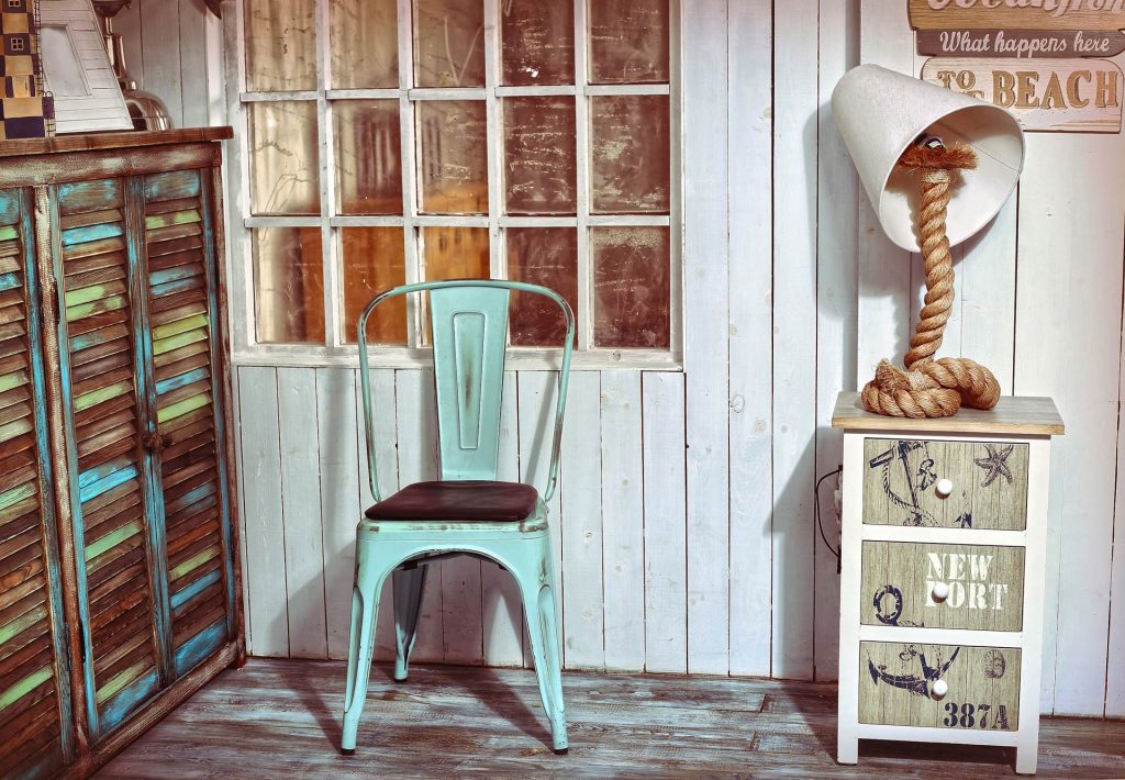 Décoration style plage avec une chaise en métal en bleu, deux meubles vintage et une lampe avec un nœud de corde comme pied.
