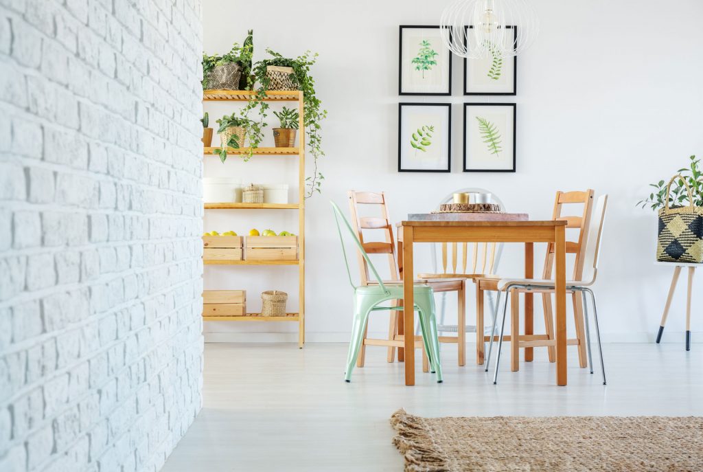 Étagère en bois naturel décorée avec des plantes vertes et des boîtes en bois à côté d’une table avec des chaises en métal et en bois, et quatre tableaux à motifs végétales derrière.