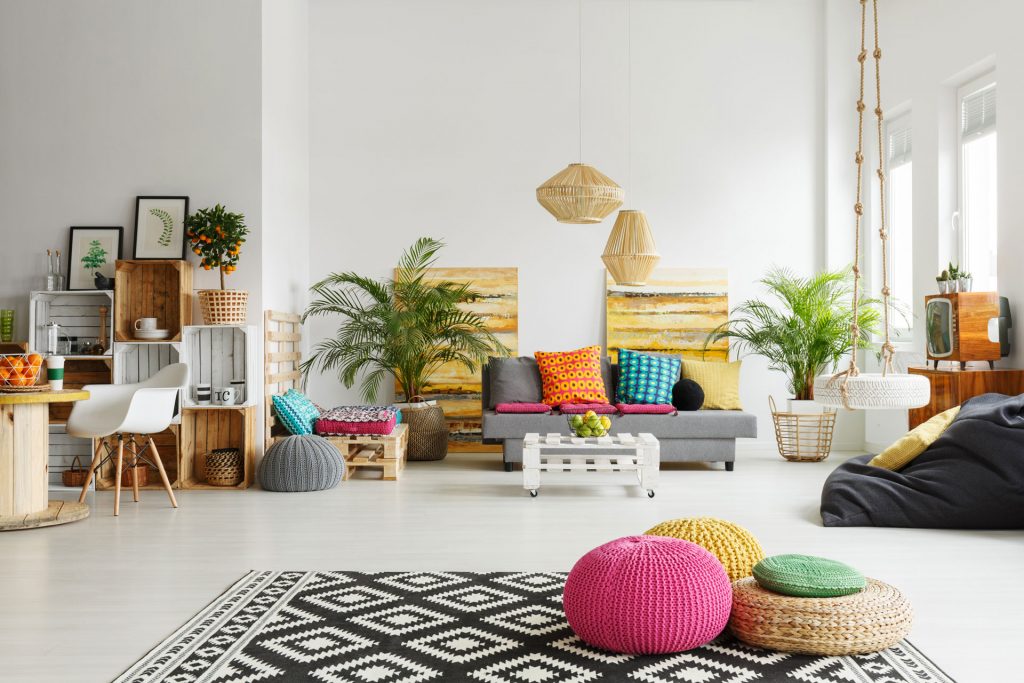 Chambre décorée avec des couleurs vives et acidulées, avec des poufs, un tapis à motifs géométriques, des meubles en palette et des plantes vertes.