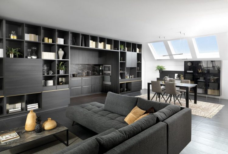 Vue de biais de la cuisine ouverte Arcos, coloris noir effet bois, avec une fenêtre sur la sous pente, une table et des chaises dans le fond et le salon en premier plan.