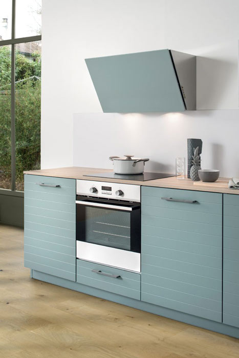 Vue de la zone de cuisson de la cuisine Multiway Arcos avec le bas four et la hotte laquée assortie aux coloris de la façade, vert clair grisé Green Tea.