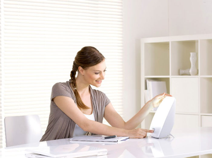 Une femme assise à un bureau blanc active un appareil de luminothérapie.
