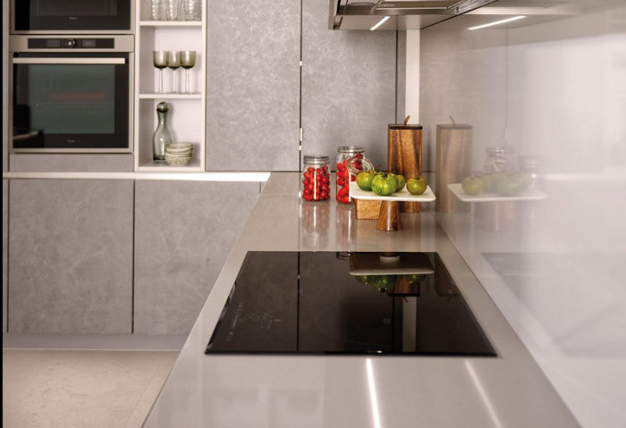 Vue latérale de la zone de cuisson de la cuisine Arcos Eolis, coloris gris, avec les profils LED allumés sous les meubles hauts.
