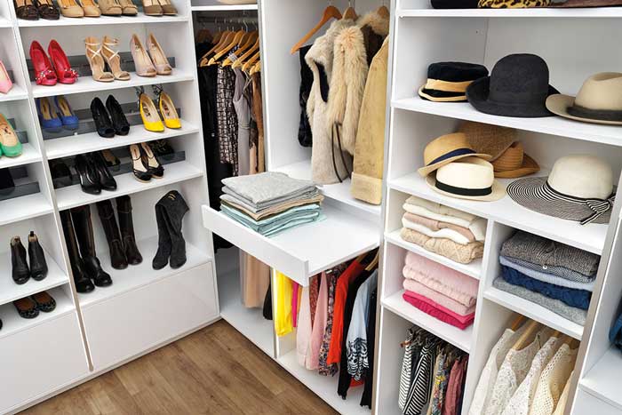 Vue sur l'angle du dressing blanc Showroom Privé, avec des étagères, de la penderie et du rangement pour les chaussures et les chapeaux.