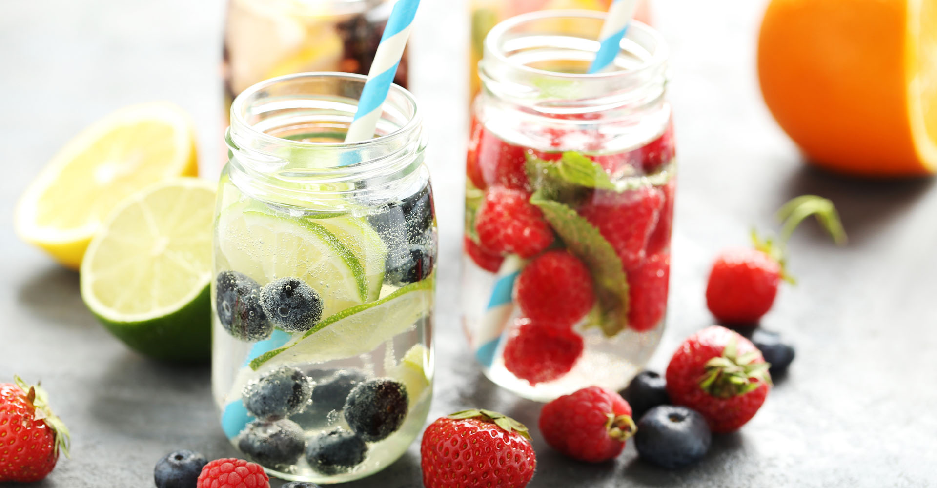 Deux bocaux avec l'eau aromatisée : une eau infusée au citron vert et aux myrtilles et l'autre aux fraises et à la menthe.