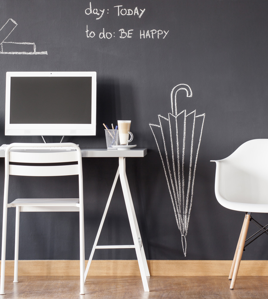 Espace bureau avec un bureau blanc et deux chaises blanches devant un mur noir avec des éléments de décoration dessinés avec une craie blanche.