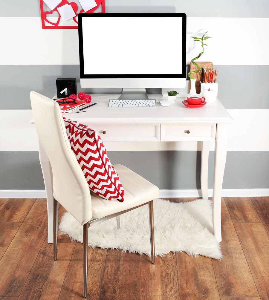 Espace bureau avec un bureau et chaise blancs décoré avec des éléments en rouge, un tapis sous la table et un mur à rayures grises et blanches.