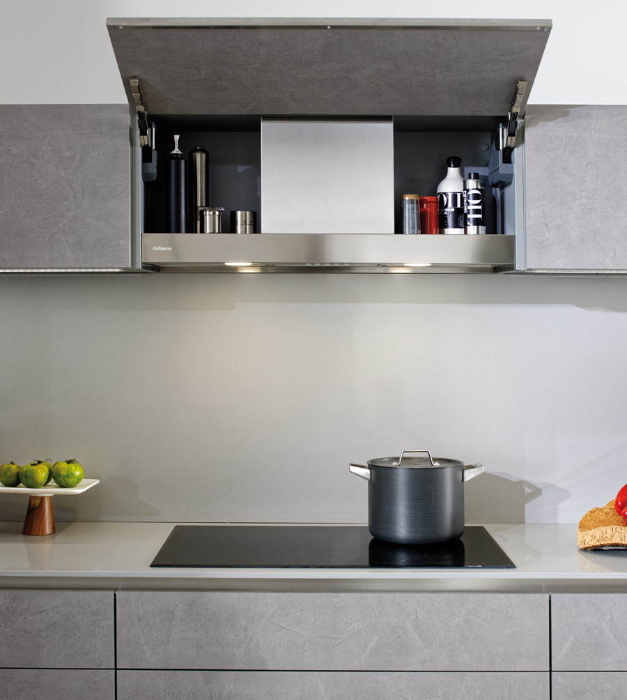 Vue du meuble haut avec la hotte cachée ouvert dans une cuisine grise.